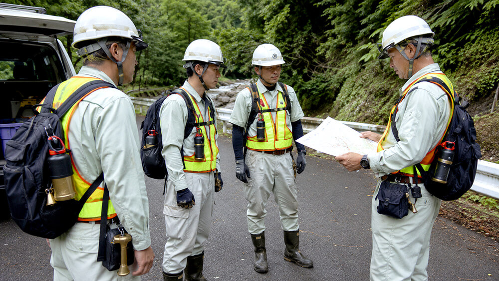 山間部の点検作業を複数人で行うイメージ