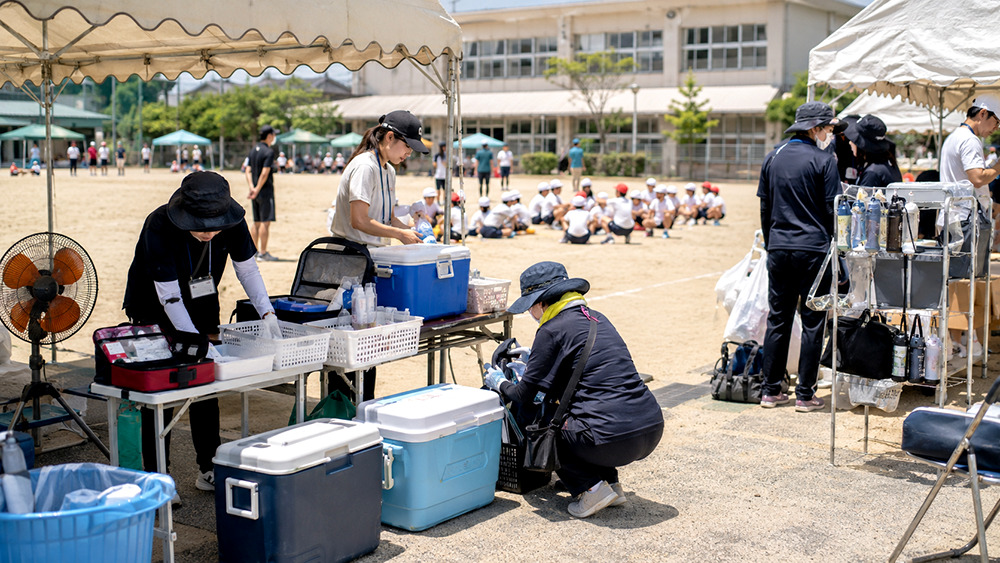 運動会会場でテントやクーラーボックスを準備する学校スタッフ